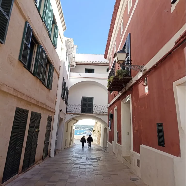 Narrow European alley with colorful buildings and two people walking toward a scenic ocean view.