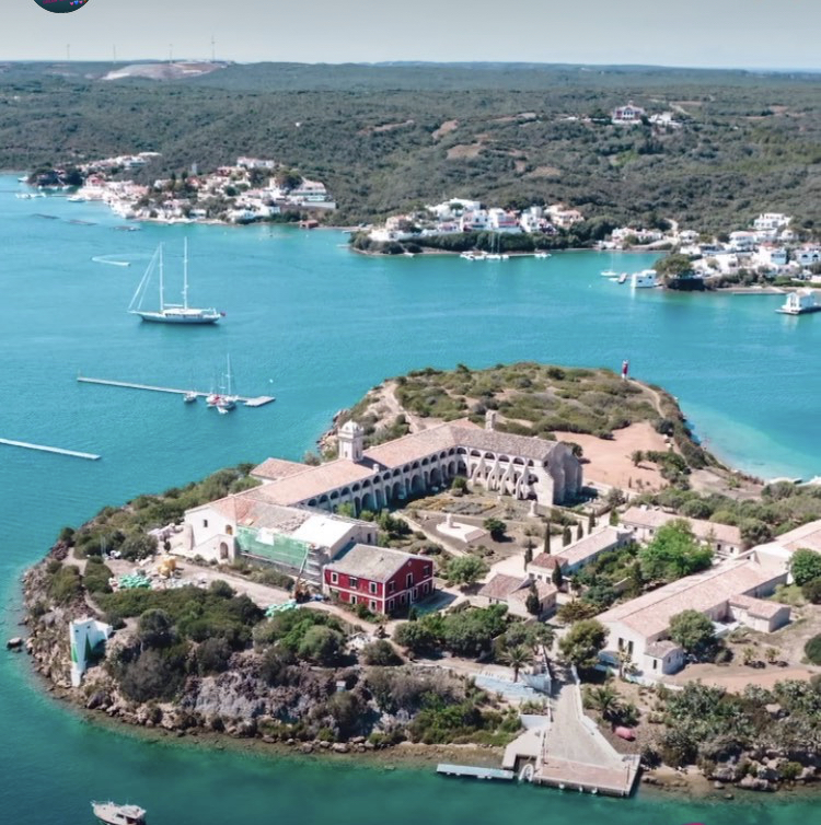 Scenic aerial view of an island with historic buildings surrounded by turquoise waters and sailboats.