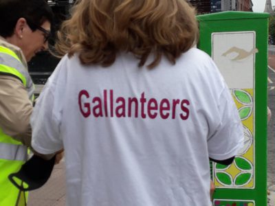 Person wearing a Gallanteers shirt next to a decorated utility box on the street.